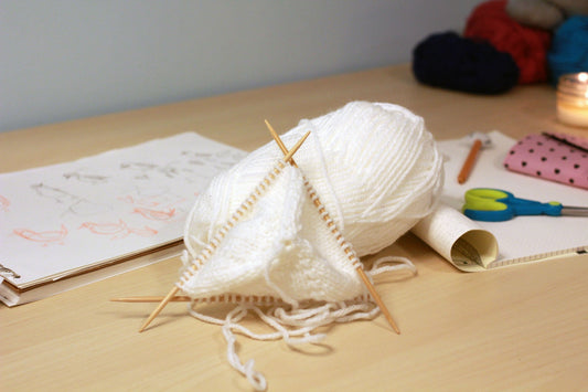 A white skein of yarn on a maple table with a knitting project on top of it.